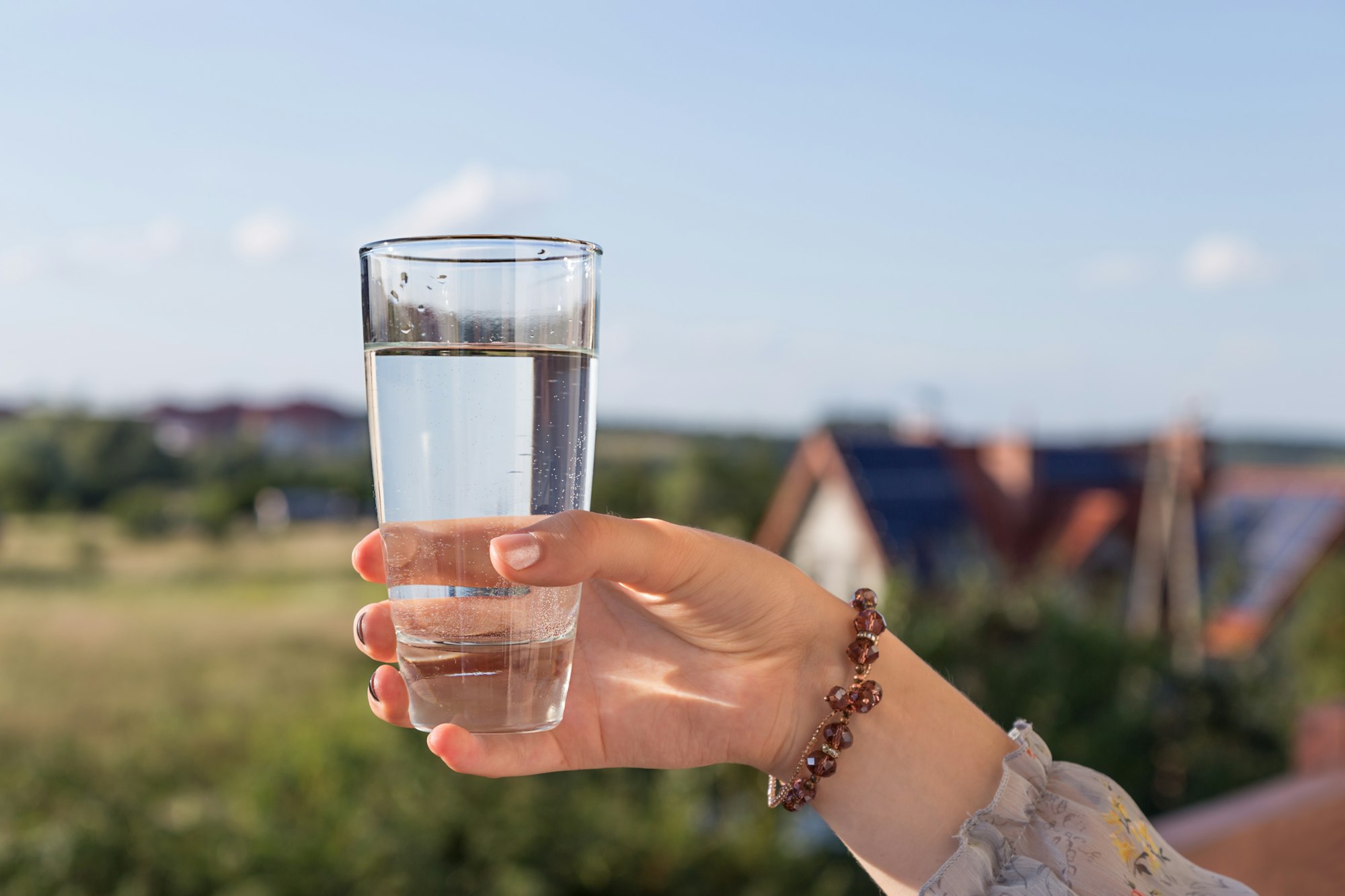 A woman's hand holds a glass of drinking water against a natural background